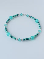 A beaded bracelet featuring turquoise and teal beads, interspersed with silver-colored accents. The bracelet has a mix of round and faceted beads, creating a delicate and colorful accessory.