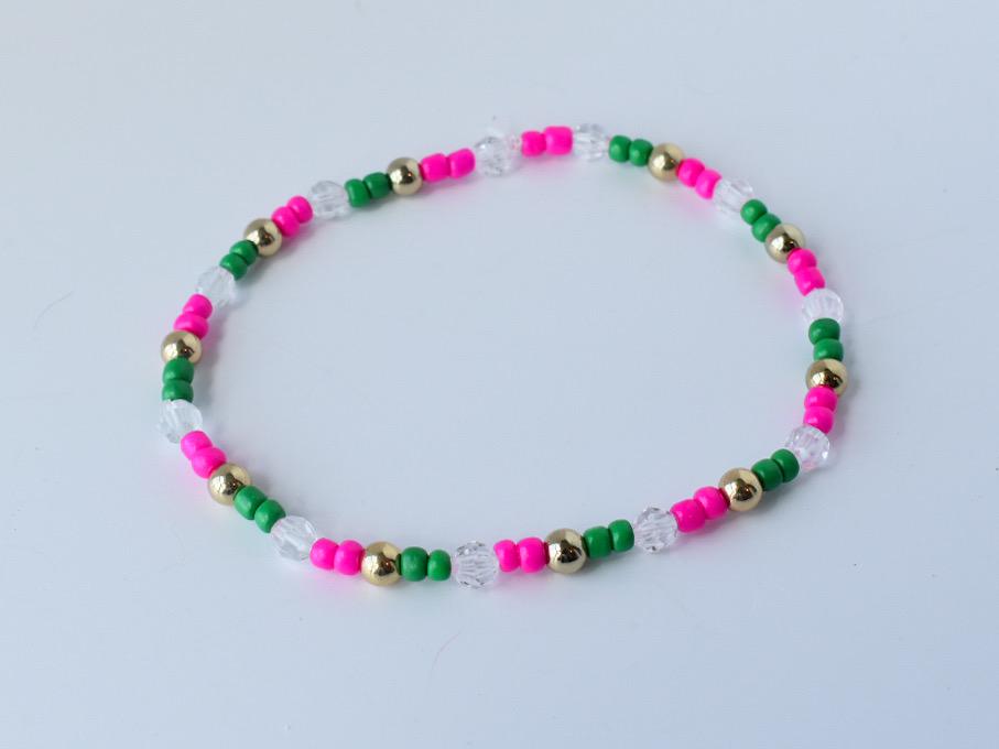 Minimalist beaded bracelet in tropical colors with alternating pink, green, and clear faceted beads, accented by gold round spacers, displayed in a simple circle.