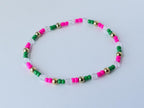 Minimalist beaded bracelet in tropical colors with alternating pink, green, and clear faceted beads, accented by gold round spacers, displayed in a simple circle.