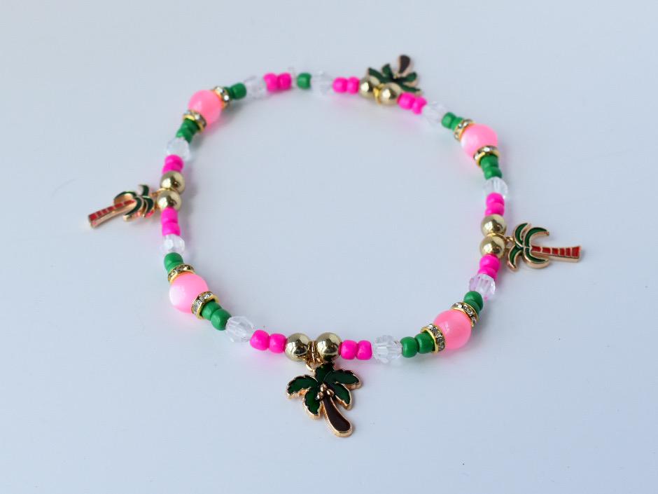 Single tropical bracelet with alternating green, pink, and clear beads, gold spacers, and multiple palm tree charms, arranged in a circle on a white surface.