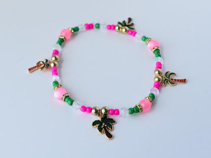 Single tropical bracelet with alternating green, pink, and clear beads, gold spacers, and multiple palm tree charms, arranged in a circle on a white surface.
