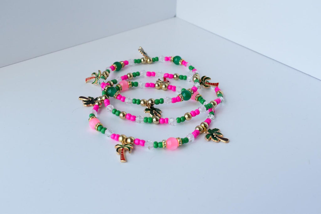 Set of colorful palm tree charm bracelets laid out in overlapping loops, featuring bright pink and green beads, gold spacer beads, and clear faceted crystals for a tropical vibe.