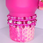 Violet Blossom tumbler bracelet stack – five beaded bracelets in varying shades of pink, fuchsia, and clear, with faceted glass crystals and sparkling rhinestone spacers, displayed on a stainless steel tumbler base.