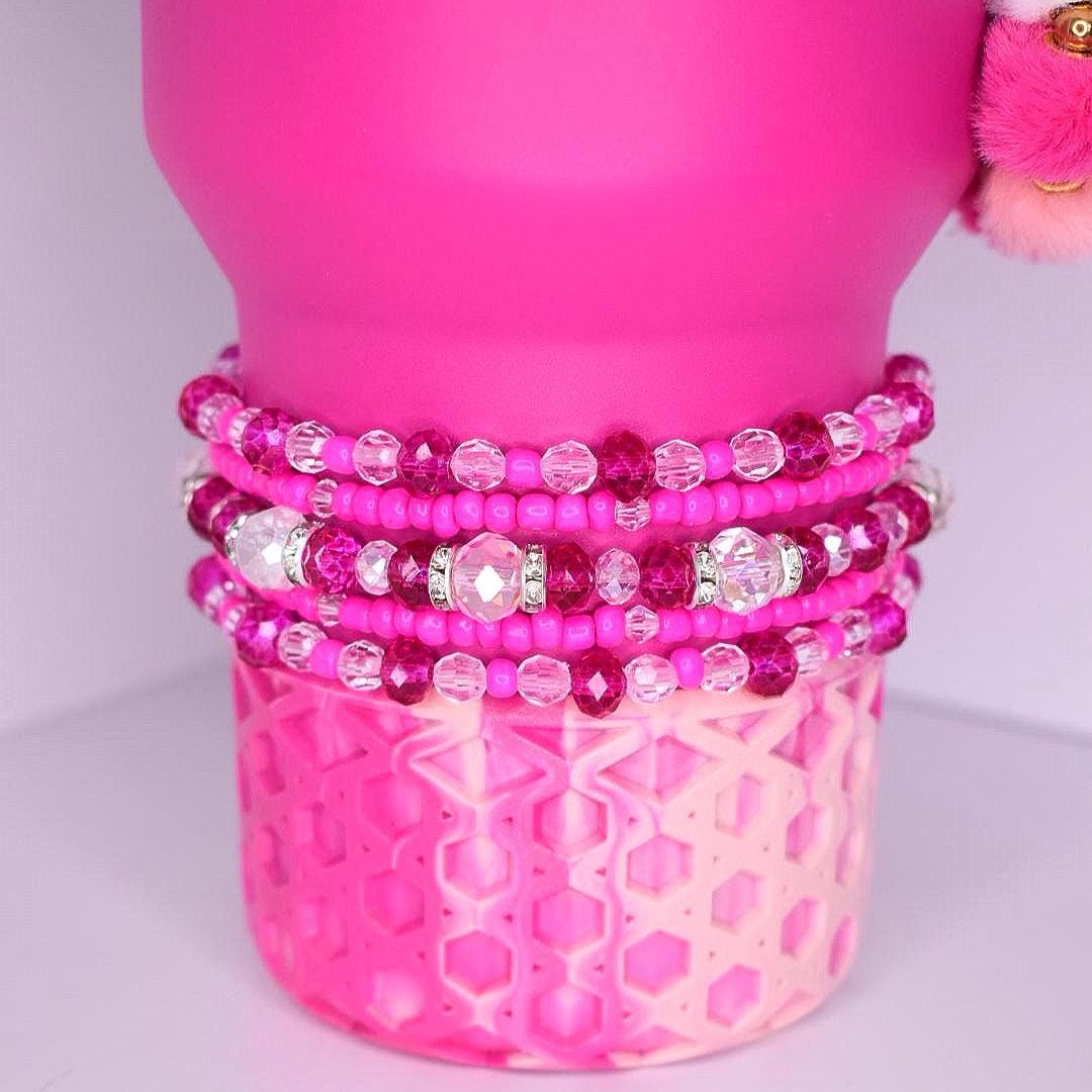 Violet Blossom tumbler bracelet stack – five beaded bracelets in varying shades of pink, fuchsia, and clear, with faceted glass crystals and sparkling rhinestone spacers, displayed on a stainless steel tumbler base.