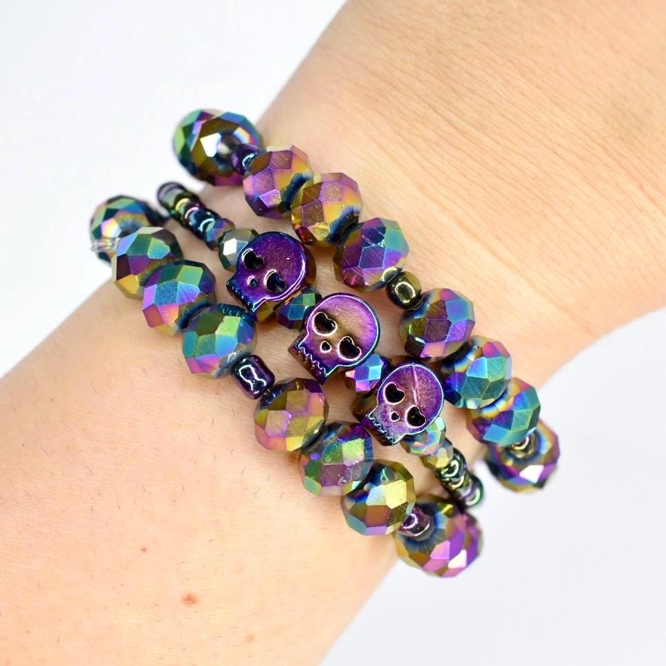 Stack of iridescent skull beaded bracelets on wrist with rainbow metallic finish