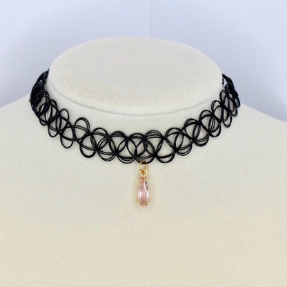 A black choker necklace with a repeating circular pattern. A teardrop-shaped, light pink gemstone pendant hangs from the center. The necklace is displayed on a white surface.