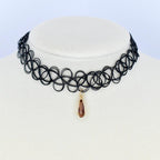 Black choker necklace with a pendant. The necklace is made of a series of interconnected loops. A teardrop-shaped pendant hangs from the center of the necklace. The pendant is a brown color and has a gold-colored bail.