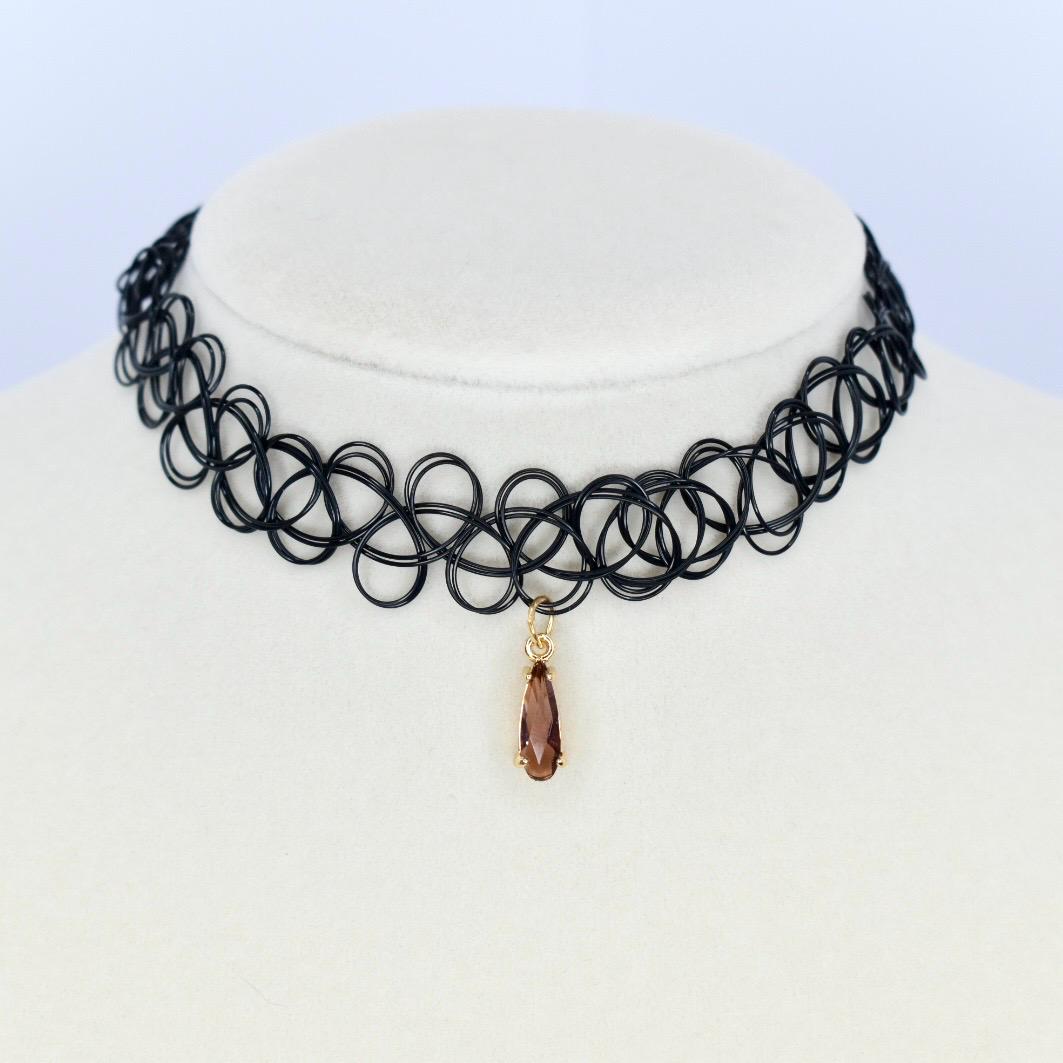 Black choker necklace with a pendant. The necklace is made of a series of interconnected loops. A teardrop-shaped pendant hangs from the center of the necklace. The pendant is a brown color and has a gold-colored bail.