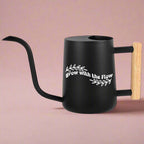Black watering can with wooden handle and white Grow with the Flow text surrounded by leaf graphics perfect calming gift for plant lovers and self-care moments