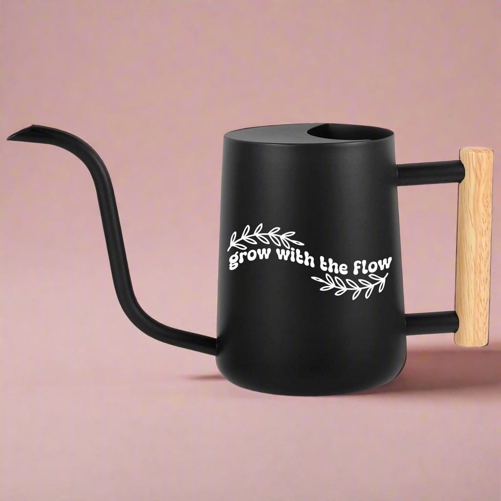 Black watering can with wooden handle and white Grow with the Flow text surrounded by leaf graphics perfect calming gift for plant lovers and self-care moments