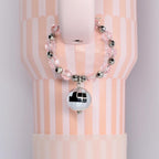 A pink and white striped tumbler with a beaded handle charm bracelet featuring clear pink beads and silver accents. A small, mirrored disco ball charm hangs from the bracelet, adding a touch of sparkle.