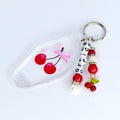 A clear keychain with a cherry design and the word 'OFFICE' spelled out in white beads. The keychain has a silver ring and a charm with red beads and a small cherry cluster. The cherry design on the keychain is red with a pink ribbon.