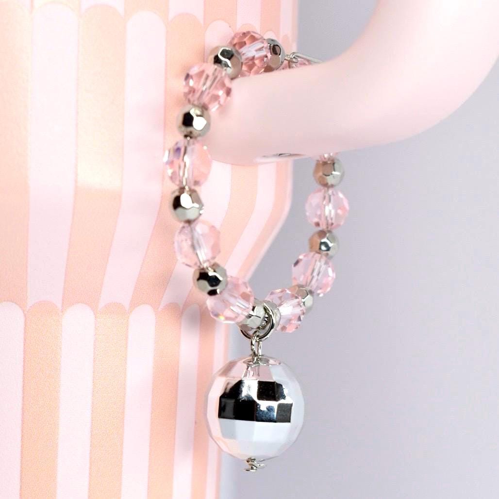 A pink beaded tumbler handle bracelet with silver accents and a disco ball charm. The bracelet features clear, faceted beads and silver-colored metal beads. The disco ball charm is round and reflective, hanging from a silver-colored clasp.