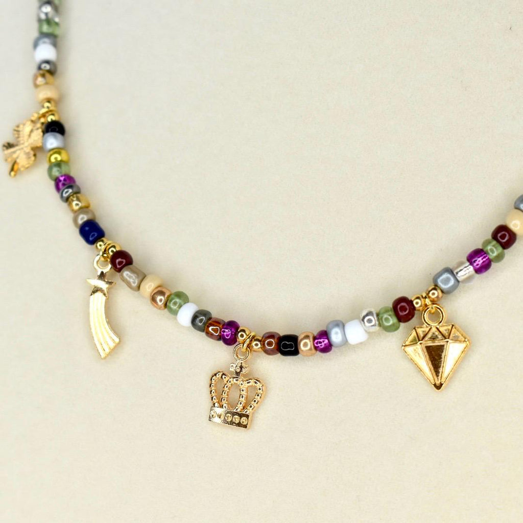 A beaded necklace with a variety of colorful beads. The necklace features gold-colored charms, including a crown, a diamond, and a shooting star. The beads are in shades of green, purple, black, white, and brown.