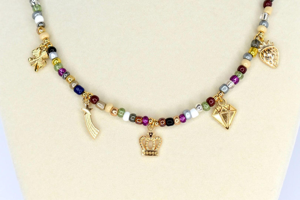 A beaded necklace with a variety of colorful beads and gold-colored charms. The charms include a crown, a diamond, a shooting star, a strawberry, and a four-leaf clover. The necklace is displayed on a white surface.