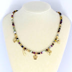 A beaded necklace with a variety of colorful beads and gold-colored charms, including a crown, a diamond, a four-leaf clover, a heart, and a feather. The necklace is displayed on a white mannequin.