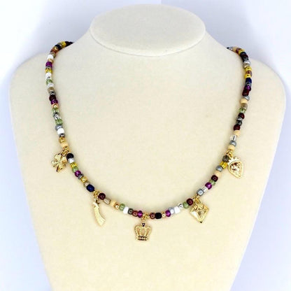 A beaded necklace with a variety of colorful beads and gold-colored charms, including a crown, a diamond, a four-leaf clover, a heart, and a feather. The necklace is displayed on a white mannequin.