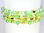A stack of beaded bracelets in shades of green, clear, and gold. The bracelets feature various bead shapes, including round, faceted, and heart-shaped beads. The gold beads add a touch of elegance to the design.