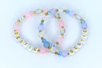 Two beaded bracelets with the word 'BESTIE' spelled out in gold letters on white beads. The bracelets feature a mix of pink, blue, and clear beads with gold accents. The beads are arranged in a circular pattern, creating a friendship bracelet design.
