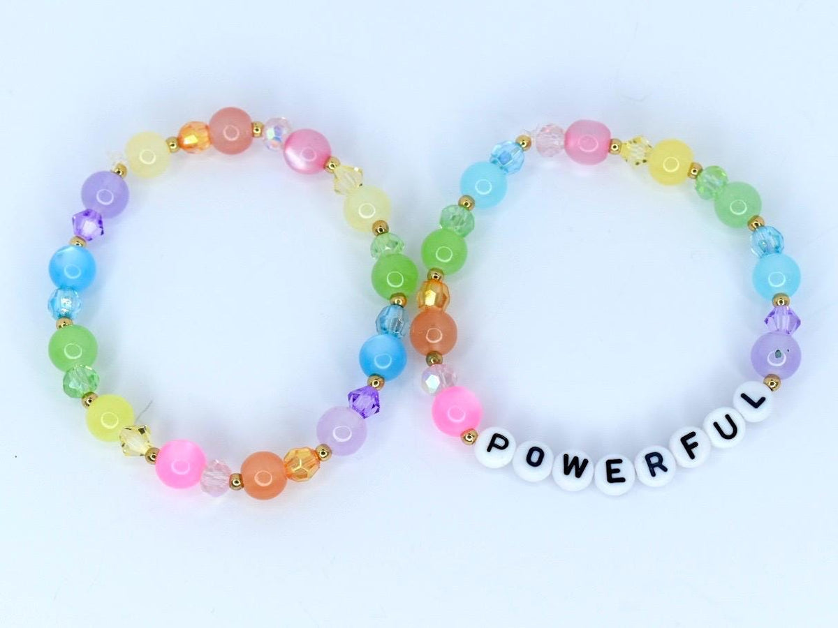 Two beaded bracelets with a rainbow of colors. One bracelet spells out the word "POWERFUL" in white letter beads. The bracelets feature a variety of colorful beads, including pink, orange, yellow, green, blue, and purple.