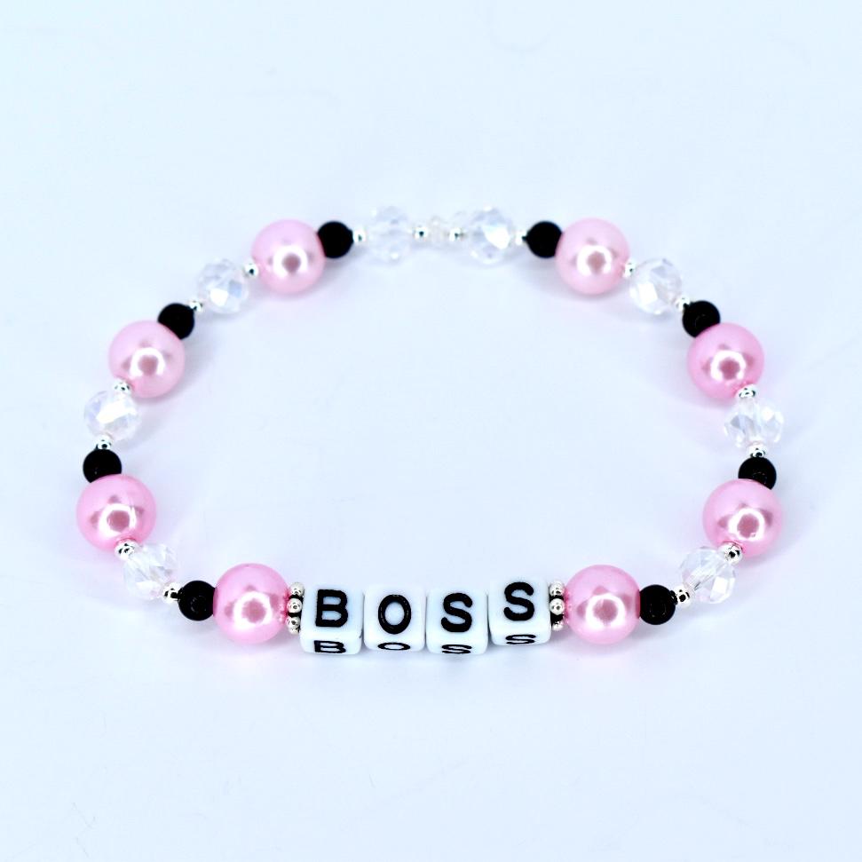A pink beaded bracelet with the word 'BOSS' spelled out in white letter beads. The bracelet features pink, black, and clear beads. The pink beads are round and the clear beads are faceted. The bracelet is on a white background.