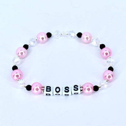 A pink beaded bracelet with the word 'BOSS' spelled out in white letter beads. The bracelet features pink, black, and clear beads. The pink beads are round and the clear beads are faceted. The bracelet is on a white background.