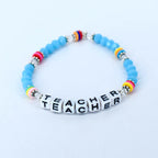 A light blue beaded bracelet with the word "TEACHER" spelled out in white letter beads. The bracelet features colorful accents of pink, yellow, and rainbow-colored beads.