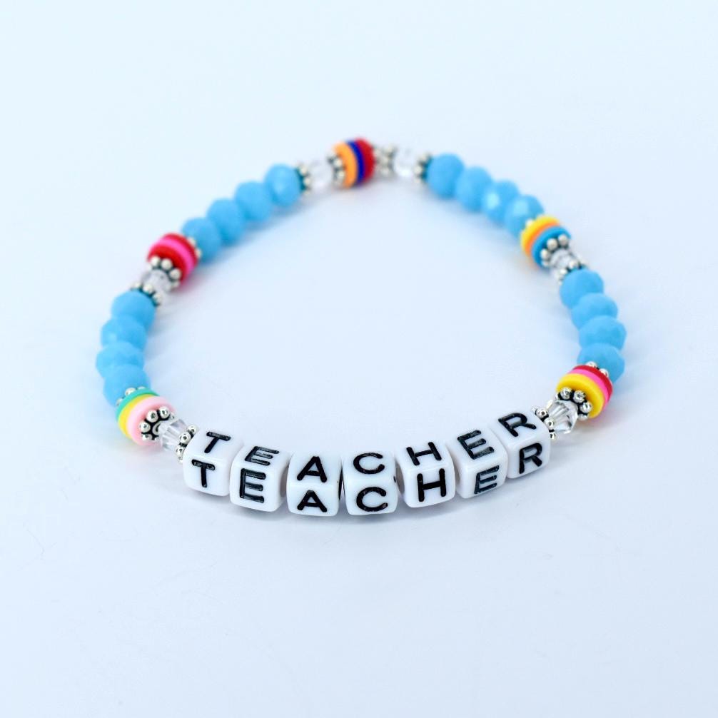A light blue beaded bracelet with the word "TEACHER" spelled out in white letter beads. The bracelet features colorful accents of pink, yellow, and rainbow-colored beads.