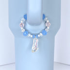 A blue and pink beaded charm bracelet with a clear, iridescent slipper pendant. The bracelet features blue, pink, and clear beads. The charm is attached to a light blue object.