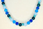 A beaded necklace featuring a gradient of blue hues. The necklace showcases a variety of round beads in shades of light blue, medium blue, and dark blue, interspersed with smaller, textured beads. The necklace is a jewelry item.