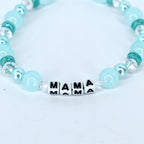 A light blue beaded bracelet with the word "MAMA" spelled out in white letter beads. The bracelet features a mix of round and faceted beads in shades of blue and clear.