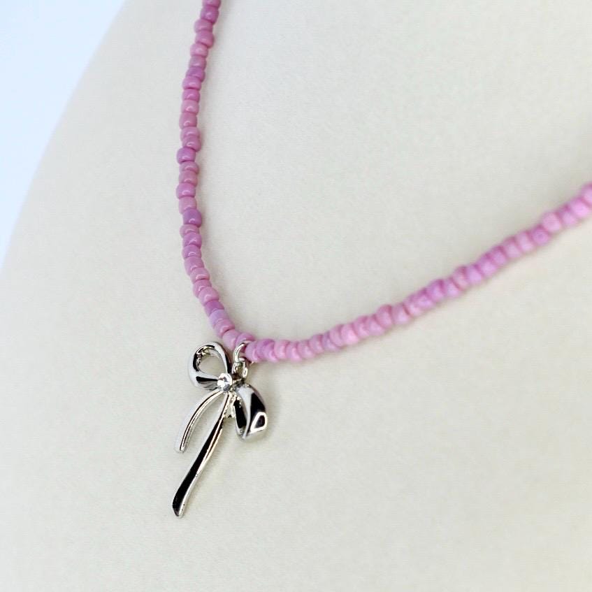 Pink seed bead necklace featuring a dainty silver bow pendant – trendy handmade jewelry gift for her.