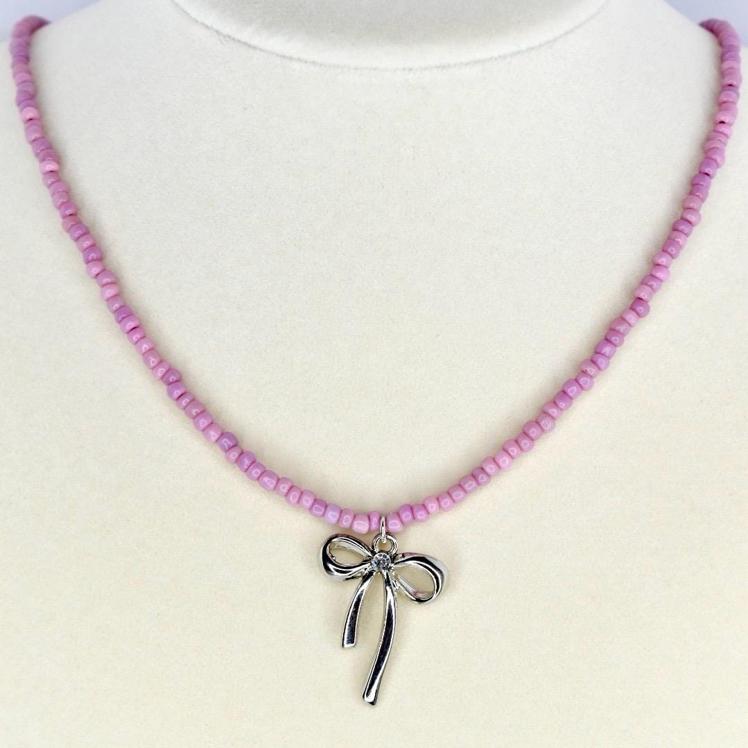 Handmade pink beaded necklace with silver bow charm – cute pastel jewelry for everyday wear.