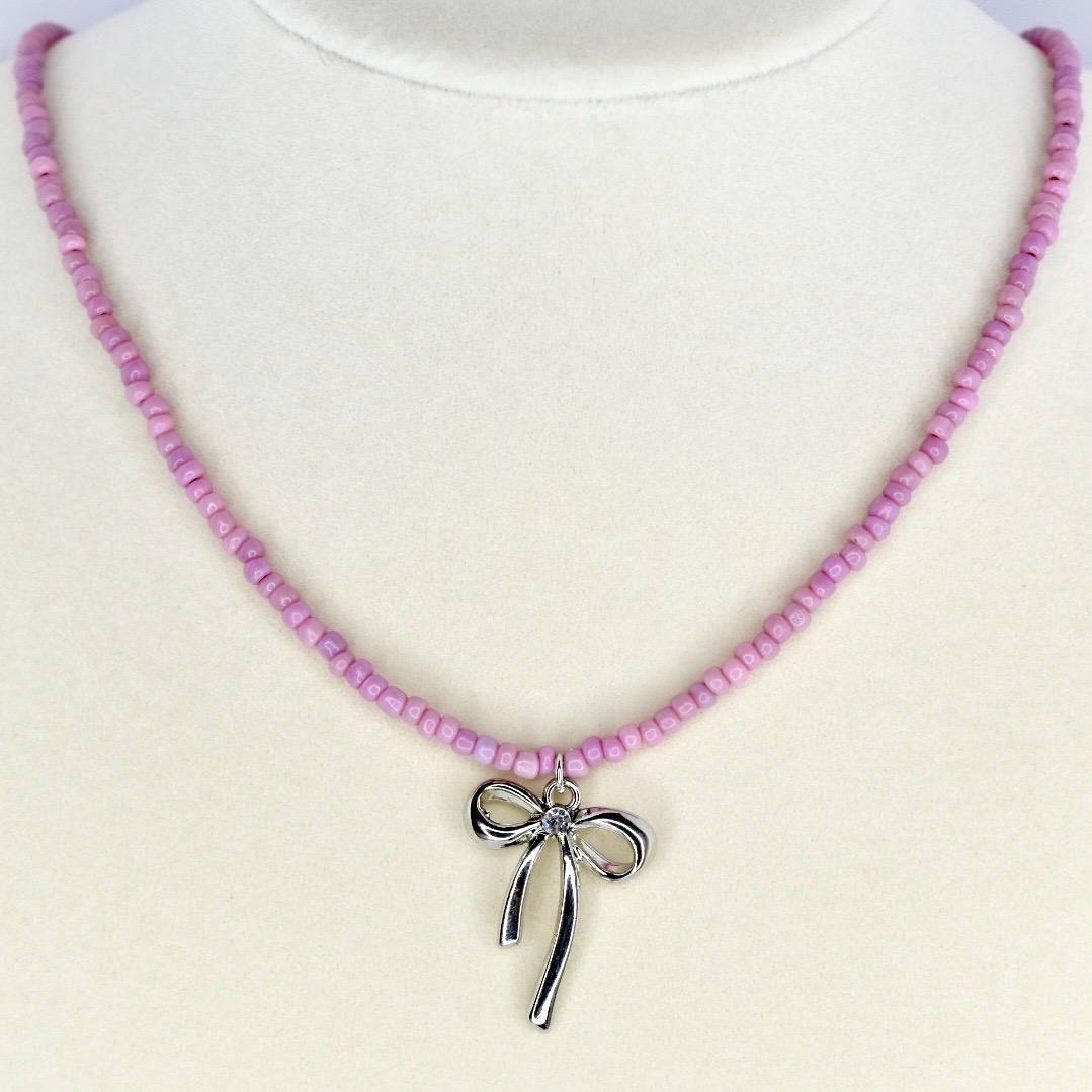 Handmade pink beaded necklace with silver bow charm – cute pastel jewelry for everyday wear.