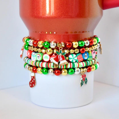 Christmas tumbler bracelet stack with red, green, gold, and silver beaded bracelets featuring holiday charms including bells, stockings, snowmen, candy canes, and holly, styled on the Scarlet Tinsel Stanley.