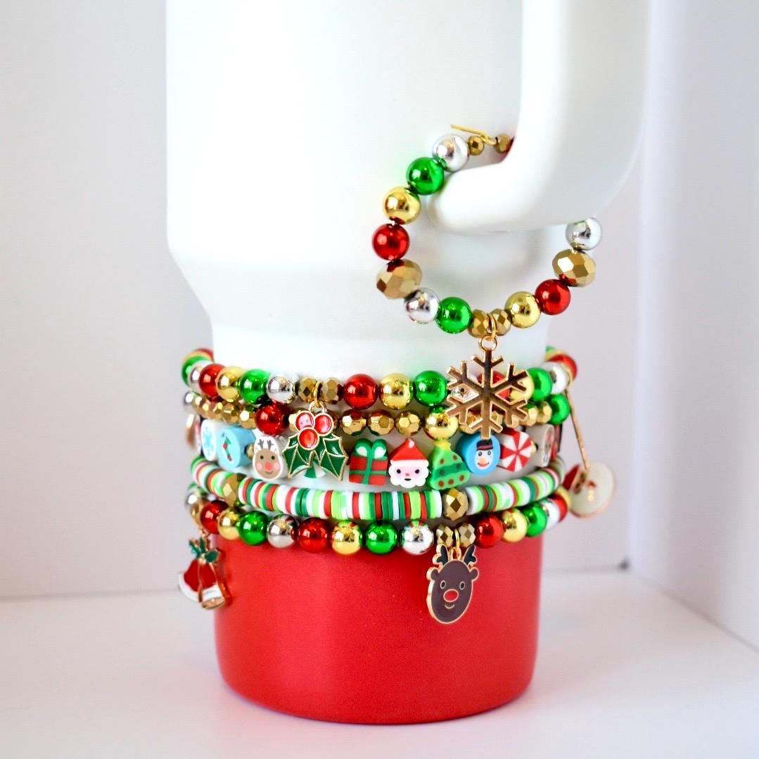 Christmas tumbler bracelet stack with 5 beaded red, green, and gold holiday bands featuring Santa, reindeer, and snowflake charms on a stainless steel tumbler.
