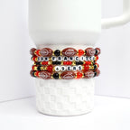 Four beaded bracelets stacked on top of each other. The bracelets feature football-shaped beads in brown, red, and black, with white letter beads spelling 'SAN FRANCISCO' and '49ERS'. Gold-colored beads add accents. The bracelets are displayed on a white, textured surface.