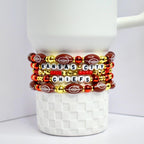 A stack of beaded bracelets featuring the Kansas City Chiefs. The bracelets are arranged on a white, textured surface. The bracelets incorporate football-shaped beads, gold beads, red beads, and white letter beads spelling out 'KANSAS CITY CHIEFS.'