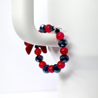 A beaded bracelet featuring alternating red and dark blue faceted beads. The bracelet is strung on a silver-colored wire and has a red bow accent. The bracelet is displayed on a white, curved surface.