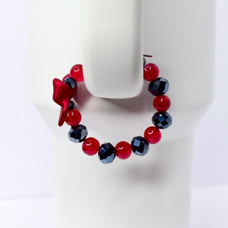 A red and black beaded bracelet with a bow charm. The bracelet features faceted black beads and round red beads. The bow charm is a deep red color. The bracelet is displayed on a white background.