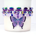Four purple and iridescent stretch bead bracelets stacked around the base of a tumbler, featuring a rhinestone butterfly charm in the center.
