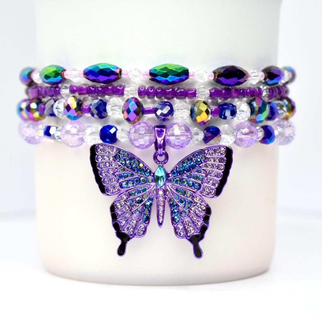 Four purple and iridescent stretch bead bracelets stacked around the base of a tumbler, featuring a rhinestone butterfly charm in the center.