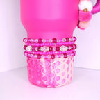 Bright pink and violet beaded tumbler bracelets with shimmering rhinestones, layered on a pink tumbler with a honeycomb-patterned silicone base.