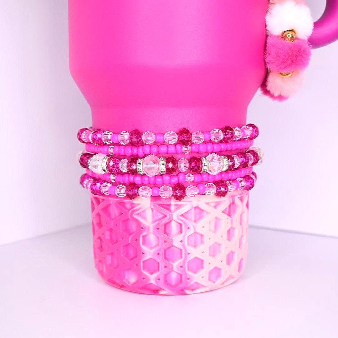 Bright pink and violet beaded tumbler bracelets with shimmering rhinestones, layered on a pink tumbler with a honeycomb-patterned silicone base.