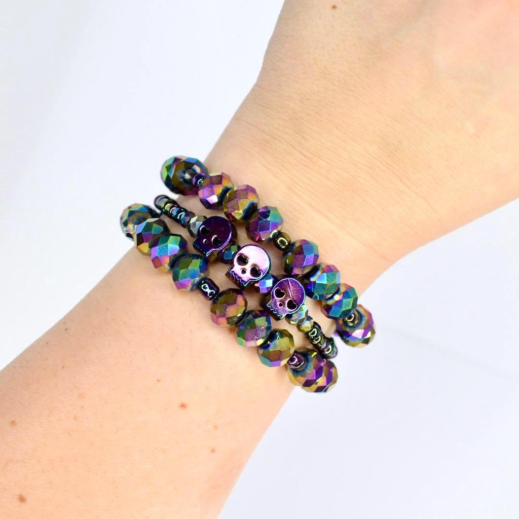 Layered crystal skull charm bracelets in holographic rainbow tones worn on arm