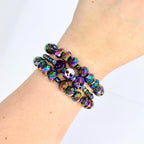 Layered crystal skull charm bracelets in holographic rainbow tones worn on arm