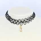 A black choker necklace with a pendant. The necklace is made of a series of interconnected black circles. A teardrop-shaped, clear crystal pendant hangs from the center of the choker. The pendant is encased in a gold-colored metal setting.