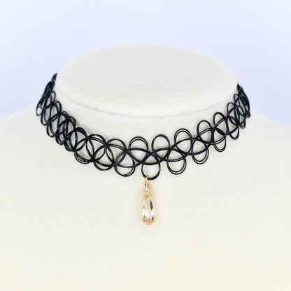 A black choker necklace with a pendant. The necklace is made of a series of interconnected black circles. A teardrop-shaped, clear crystal pendant hangs from the center of the choker. The pendant is encased in a gold-colored metal setting.