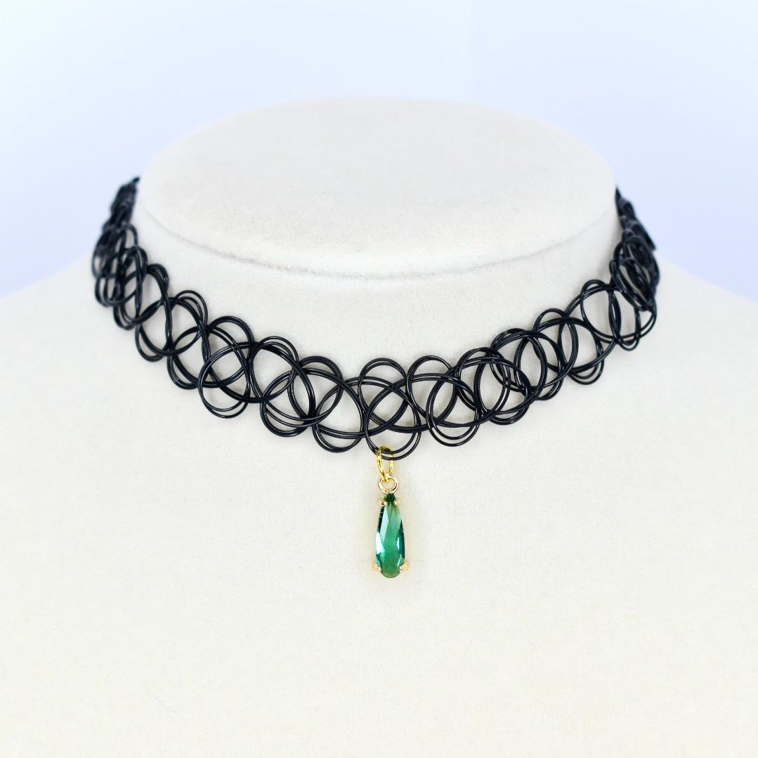 A black choker necklace with a pendant. The necklace is made of a series of interconnected black loops. A gold-colored pendant hangs from the center, featuring a teardrop-shaped green gemstone.