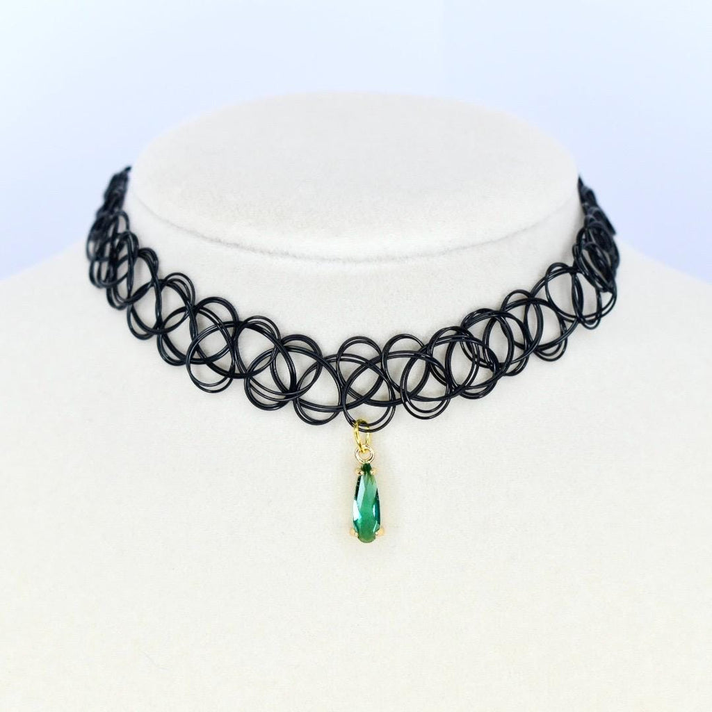 A black choker necklace with a pendant. The necklace is made of a series of interconnected black loops. A gold-colored pendant hangs from the center, featuring a teardrop-shaped green gemstone.